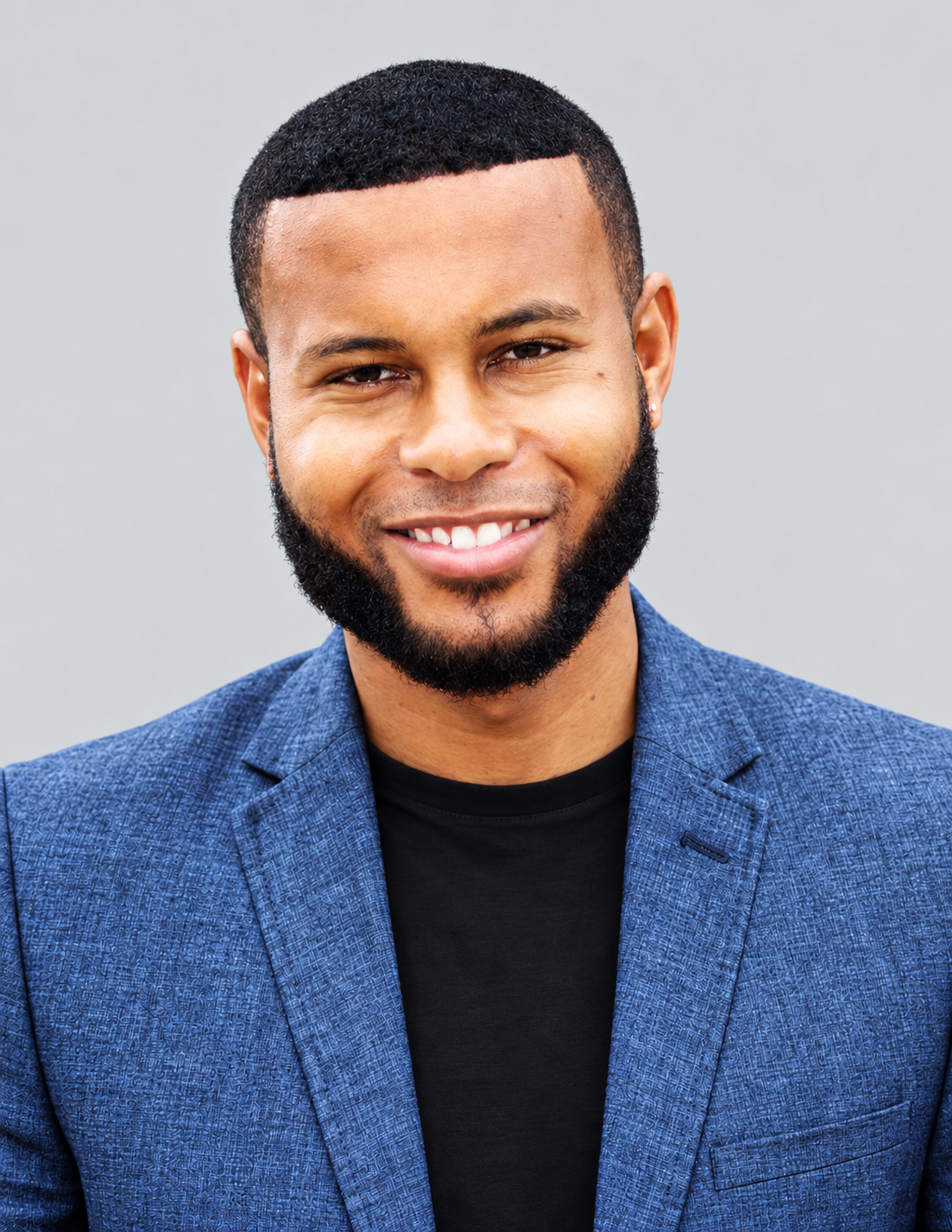 Anthony Alexander smiling in a blue blazer against a neutral gray background