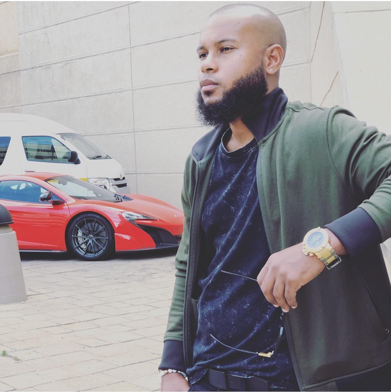 Anthony Alexander wearing a green bomber jacket and holding his glasses