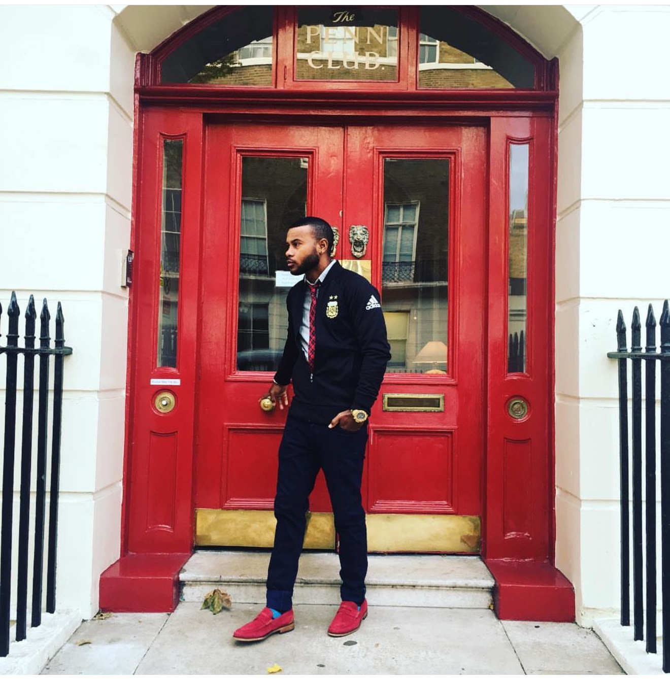 Anthony Alexander in a navy outfit and red loafers outside a red doorway