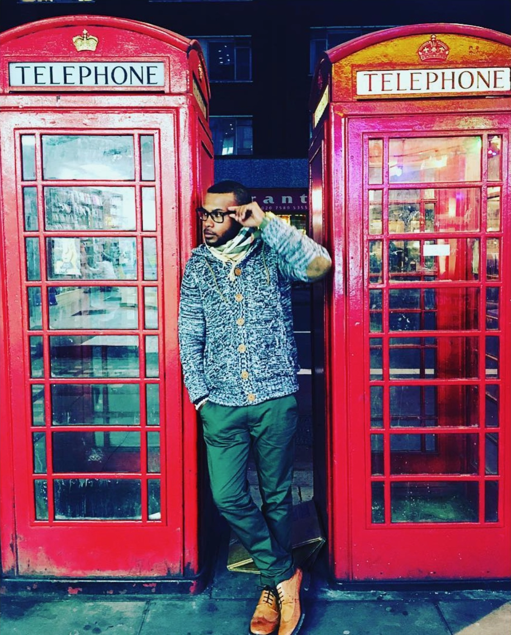 Anthony Alexander adjusting his glasses between red telephone boxes